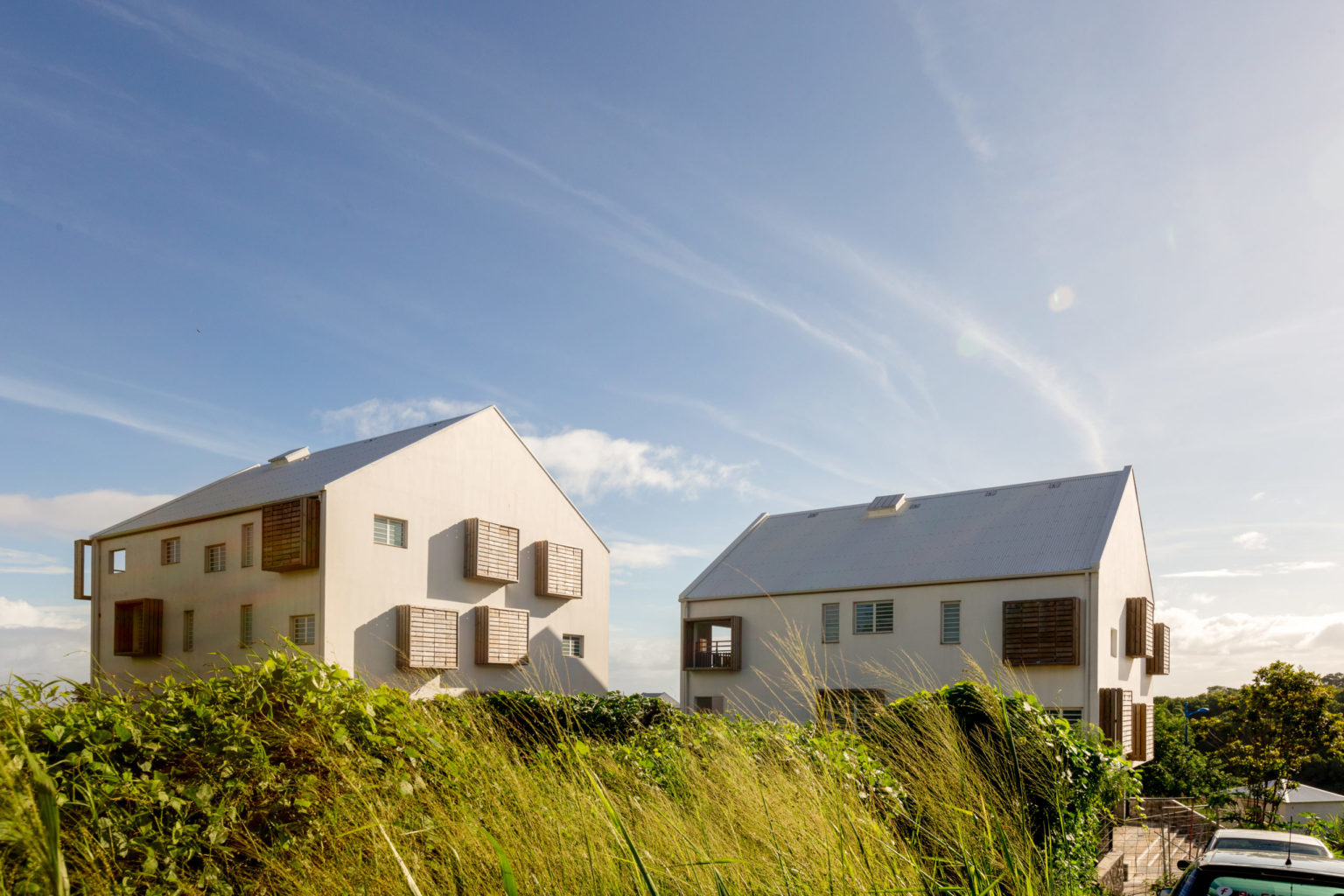 Photographie couleur représentant les façades de logements collectifs à la Réunion. De grands encadrement en bois, sur simple ou double hauteur, rythment la façade maçonnée blanche. Agence d'architecture T&T architectures