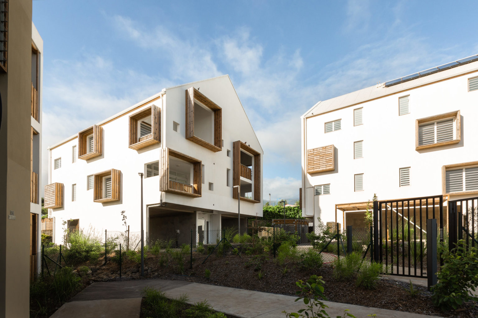 Photographies couleur représentant les façades de logements collectifs à la Réunion. De grands encadrement en bois, sur simple ou double hauteur, rythment la façade maçonnée blanche. Agence d'architecture T&T architecture