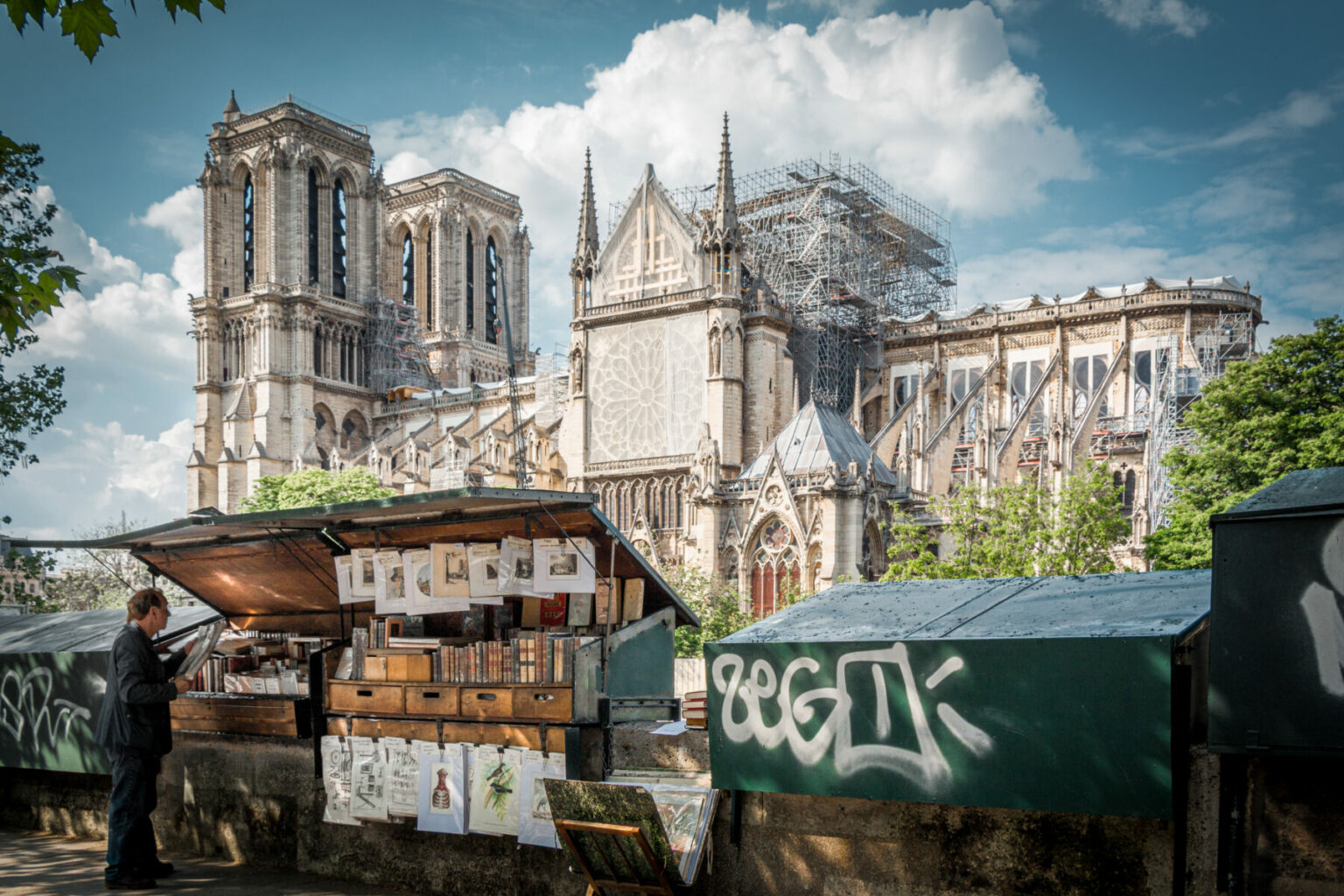 Photographie en couleur d'un bouquiniste des bords de la Seine avec dans le fond la cathédrale Notre Dame de Paris en reconstruction.